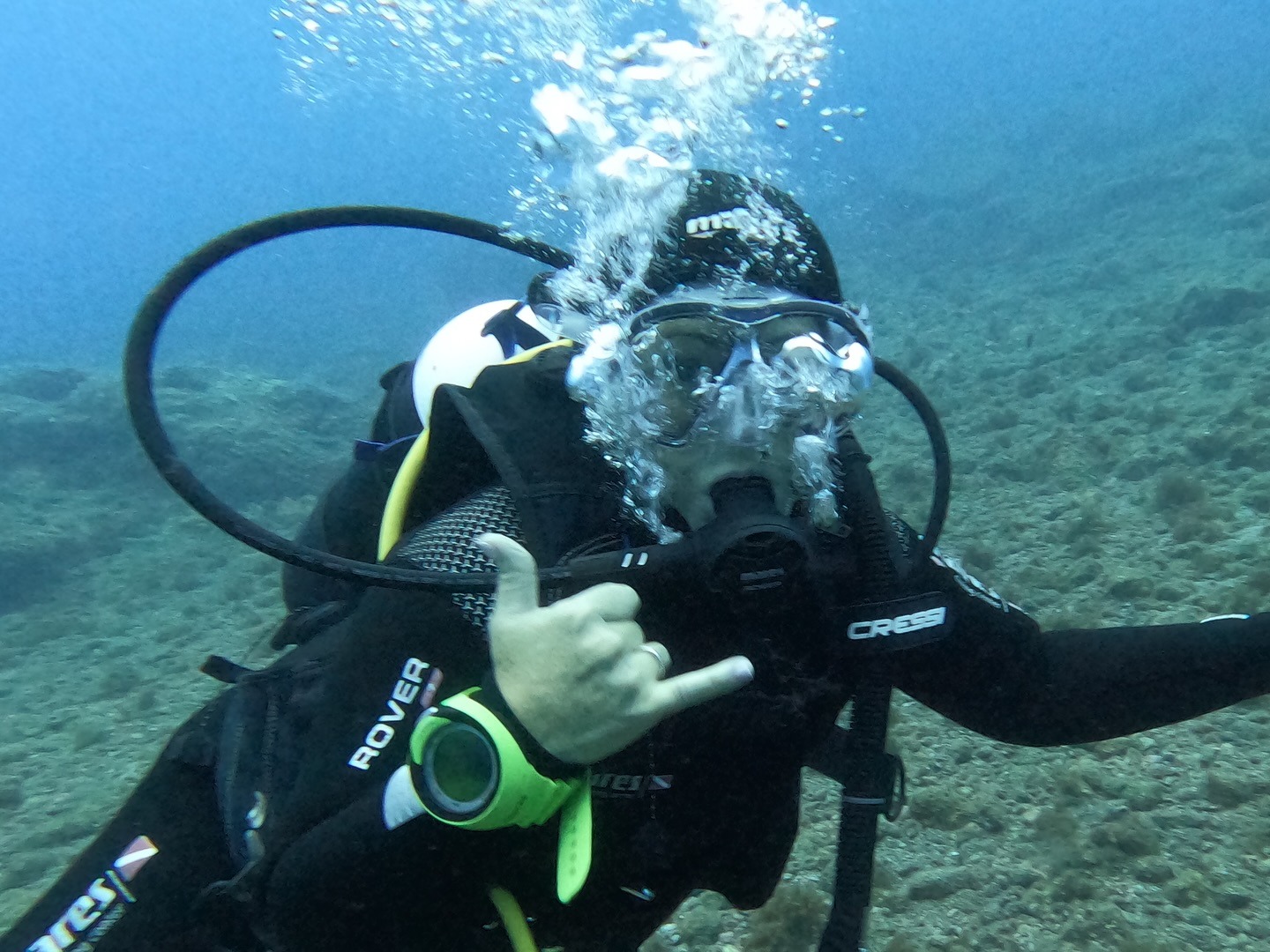 Diver underwater making a shaka sign, wearing scuba gear and surrounded by bubbles, showcasing the thrill of underwater exploration.