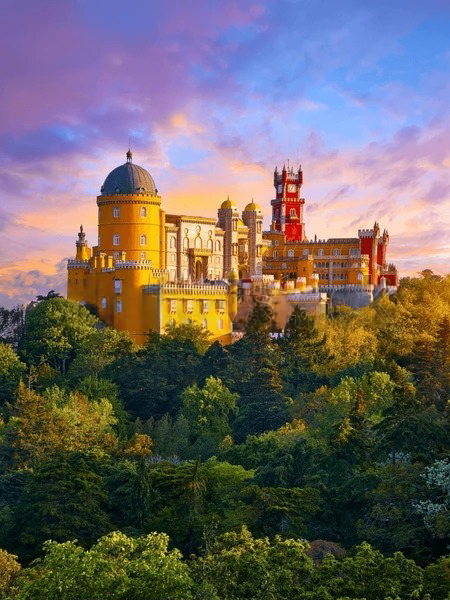 Colorful Sintra palace rises above lush green trees under a vibrant sunset sky, showcasing its unique architecture and historical significance.