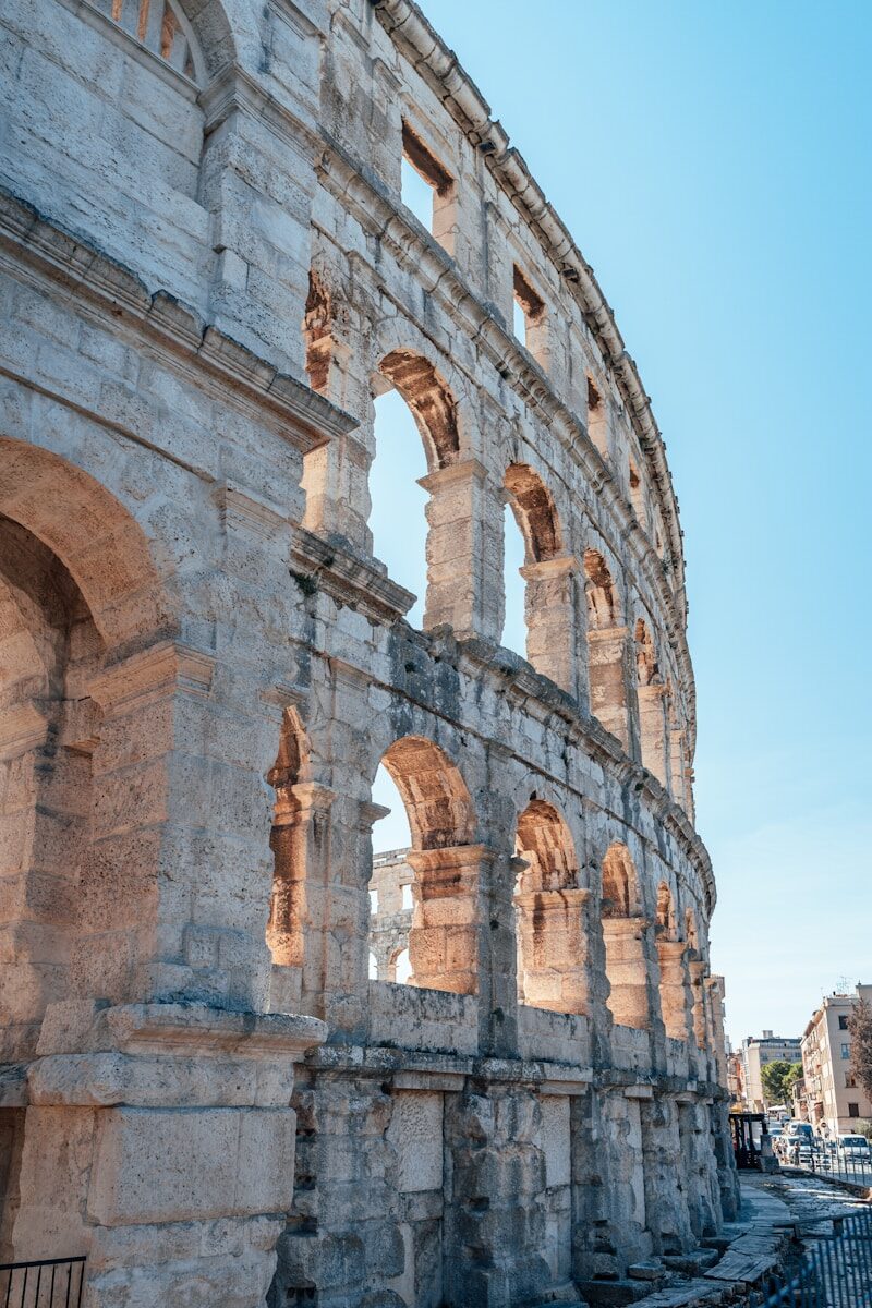 Archways and ancient stone tiers of the Roman Colosseum under a bright sky in Rome, Italy.