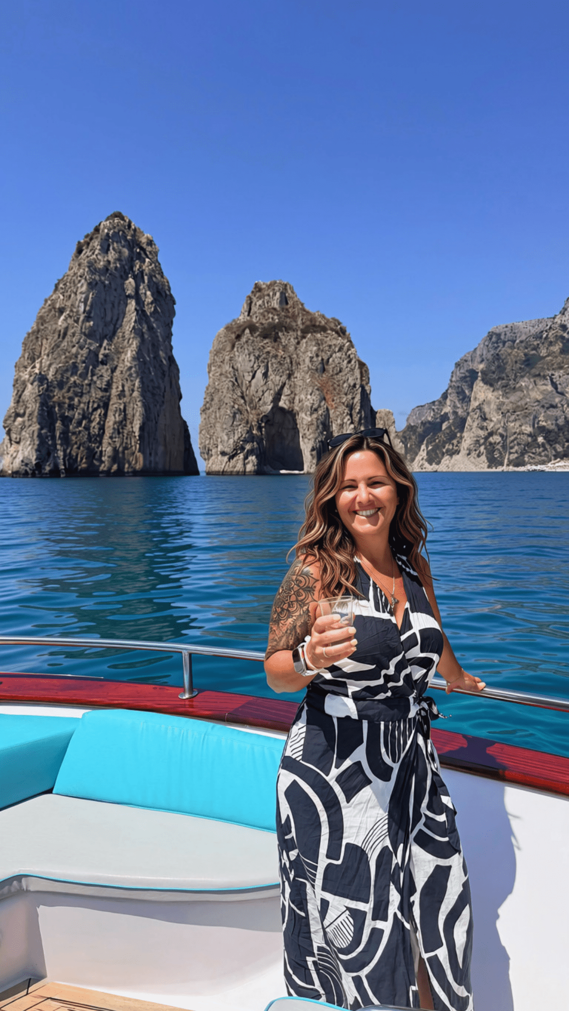 Traveler standing on a boat with the famous Faraglioni limestone sea stacks rising out of the sea in Capri, Italy.