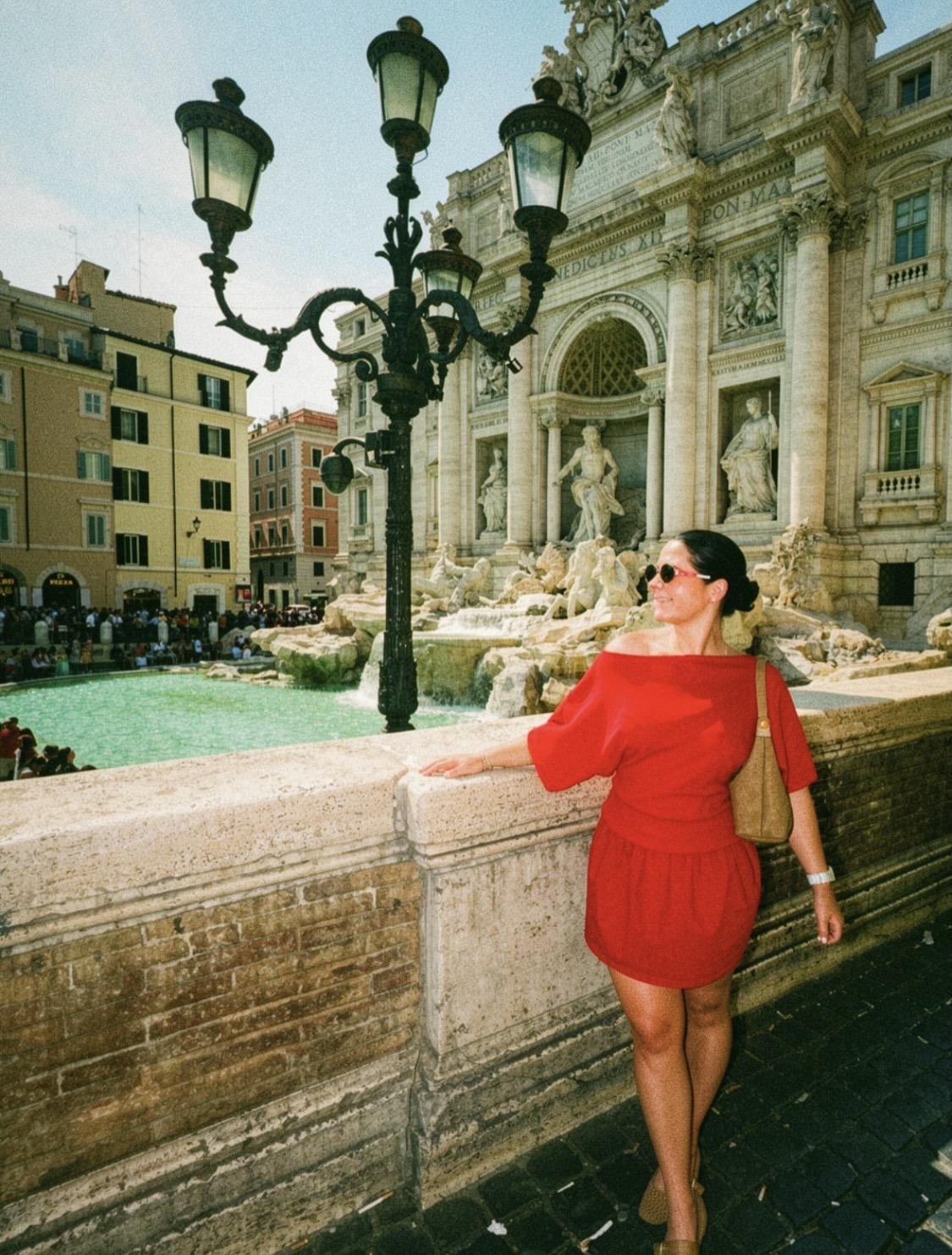 Traveler wearing a red dress standing near the stone carvings and water basin of the Trevi Fountain in Rome, Italy.